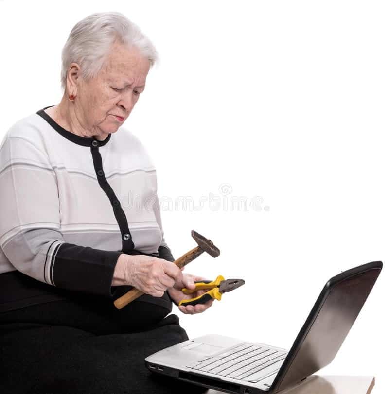 Weird stock photo of elderly woman holding hammer and pliers threatening a laptop computer