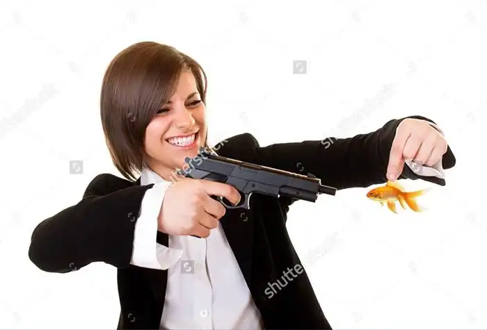 Weird stock photo of smiling businesswoman aiming handgun at dangling orange goldfish
