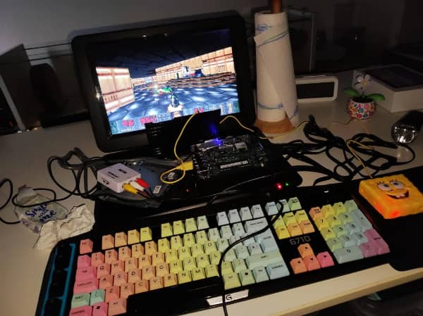 Chaotic gaming desk with rainbow mechanical keyboard Spongebob mousepad and tangled cables everywhere