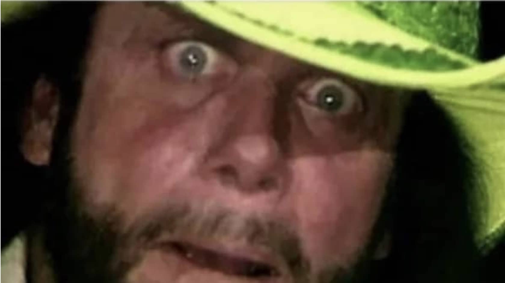 Close up intense reaction meme of professional wrestler Macho Man Randy Savage staring under a cowboy hat.