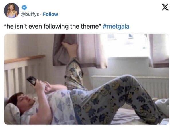 A relatable 2026 Met Gala meme showing a man lying in bed in Minion-themed pajamas staring at his phone, captioned "he isn't even following the theme."