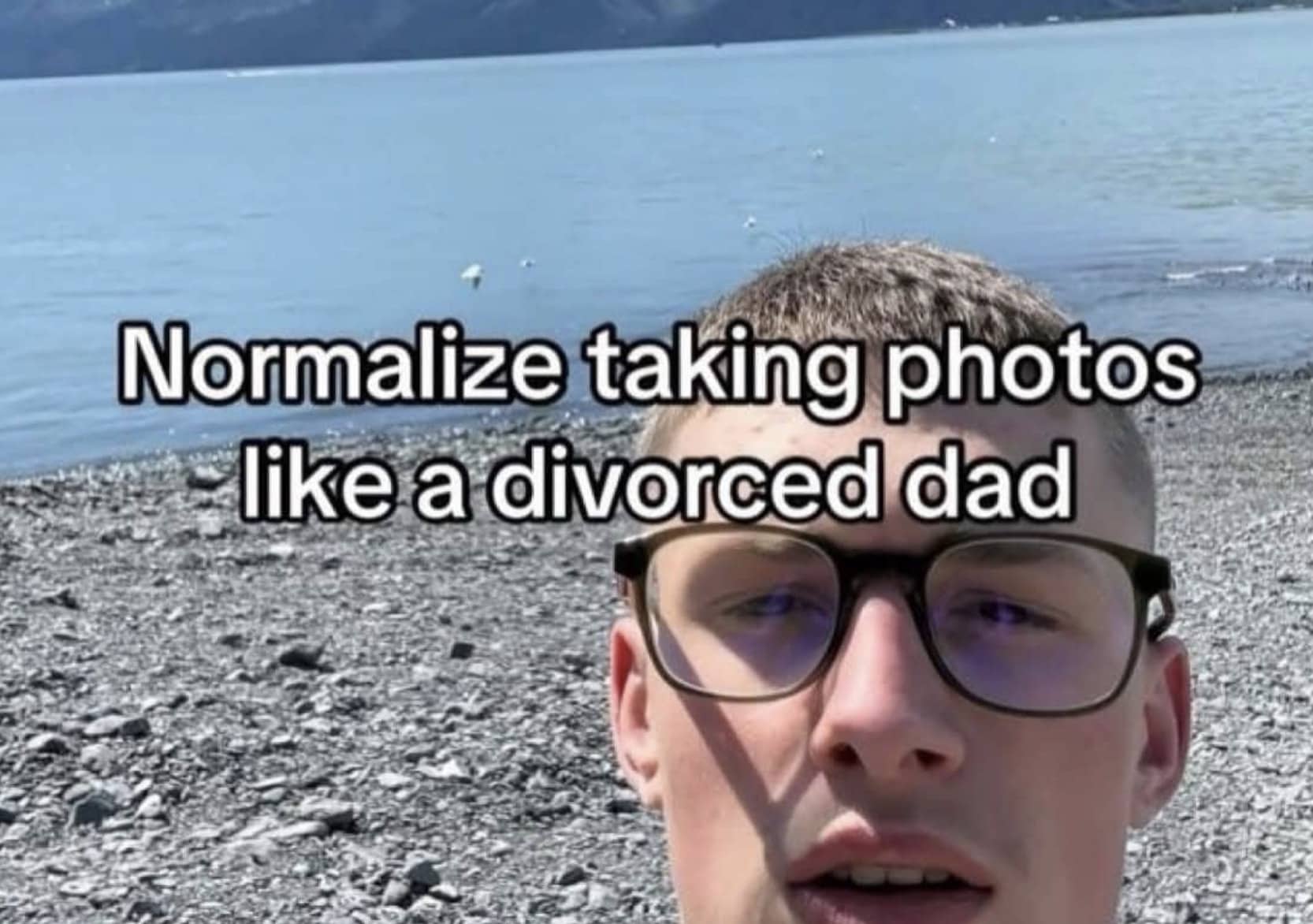 Close-up selfie of man wearing glasses at rocky beach captioned normalize taking photos like divorced dad.