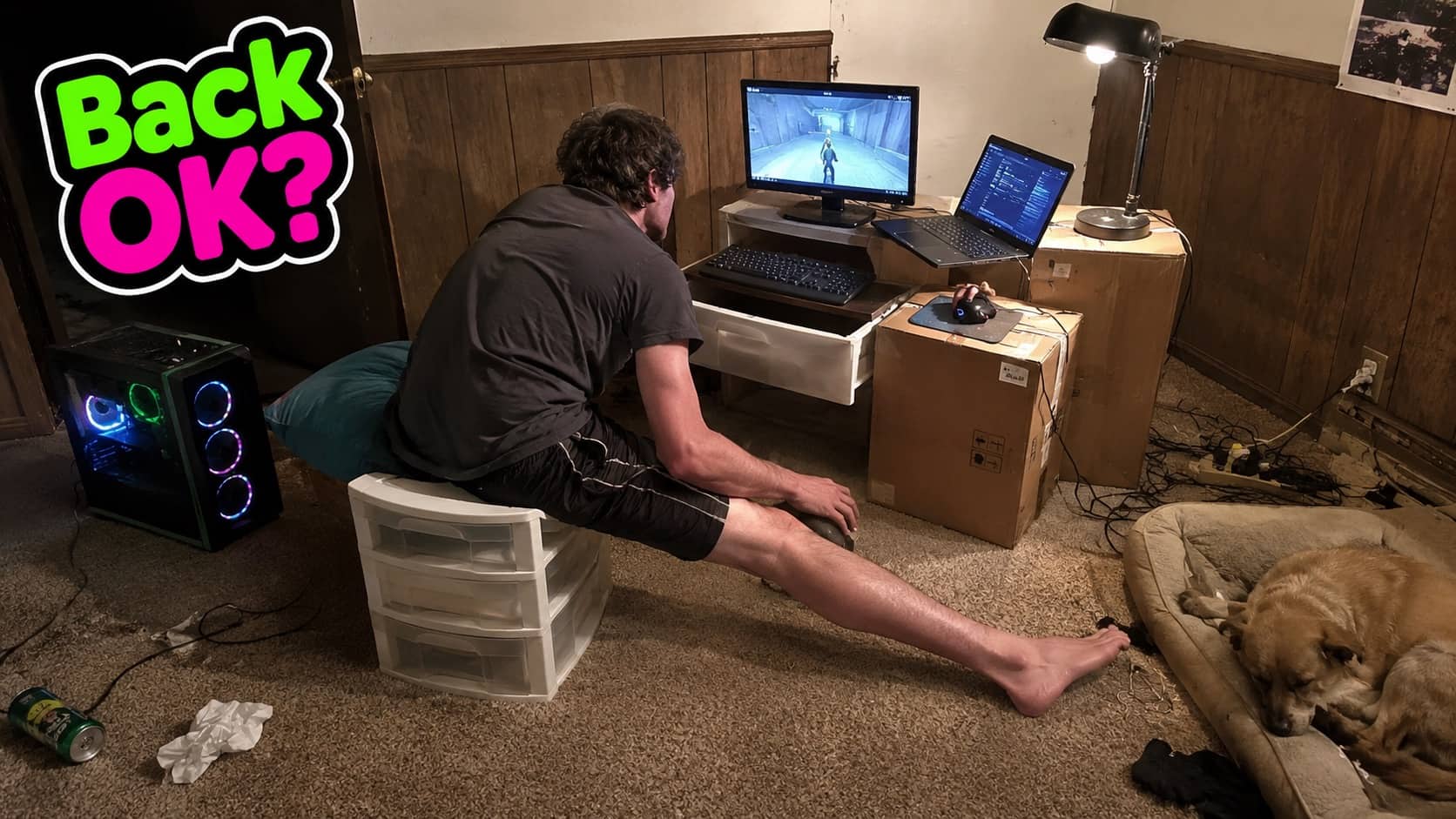 Gamer sitting on plastic drawers in a messy room using cardboard boxes as a computer desk.