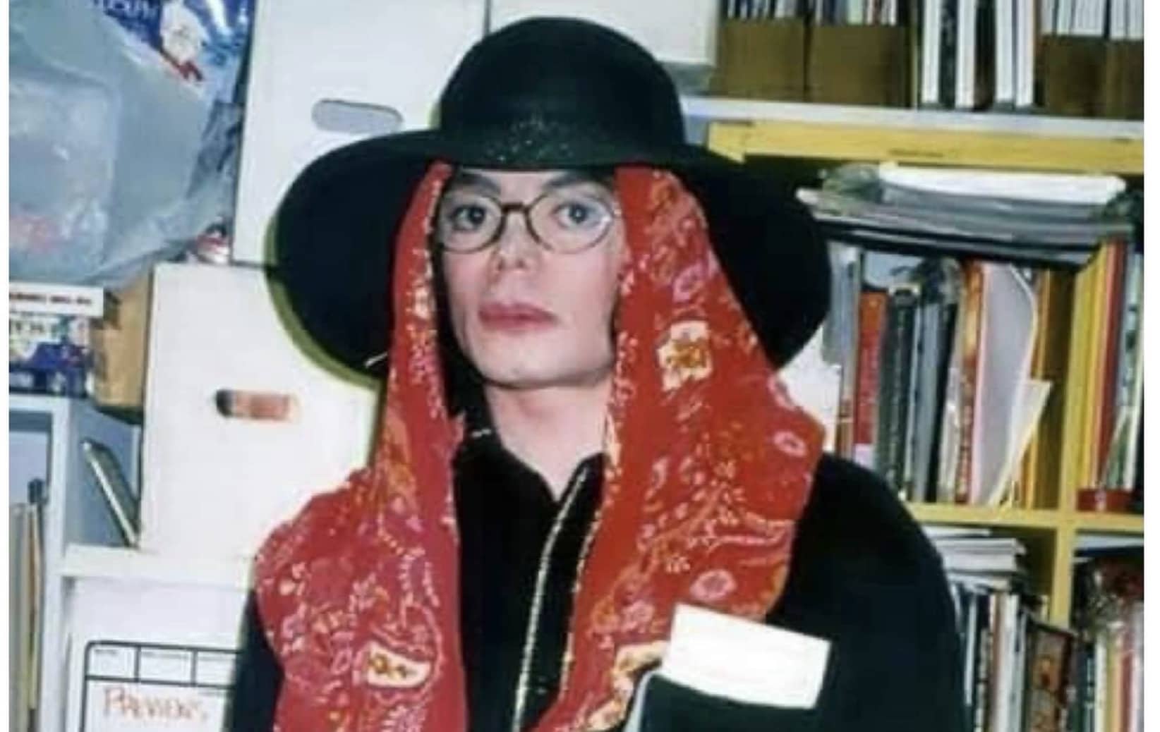 Michael Jackson wearing a black hat, clear glasses, and a red patterned headscarf indoors.