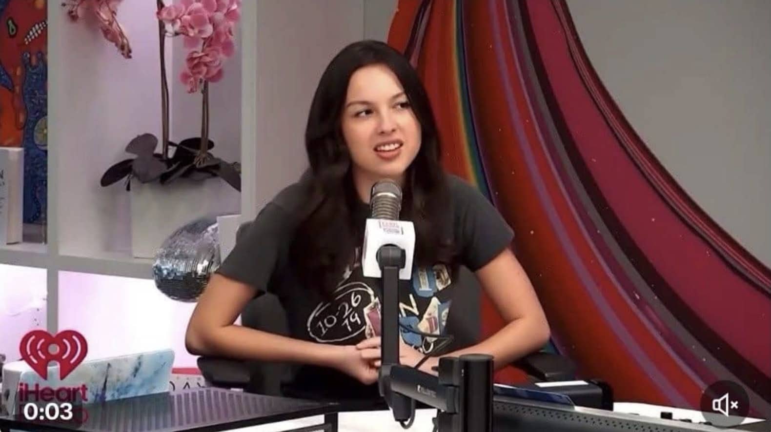 Singer Olivia Rodrigo speaking into a microphone during an interview at an iHeartRadio studio.