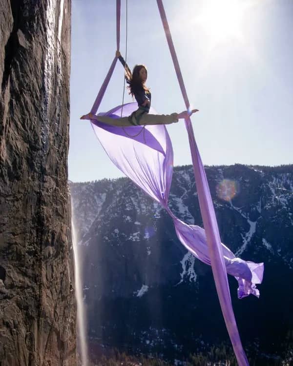 Silhouetted aerial silk performer executing a split over a snowy mountain range.