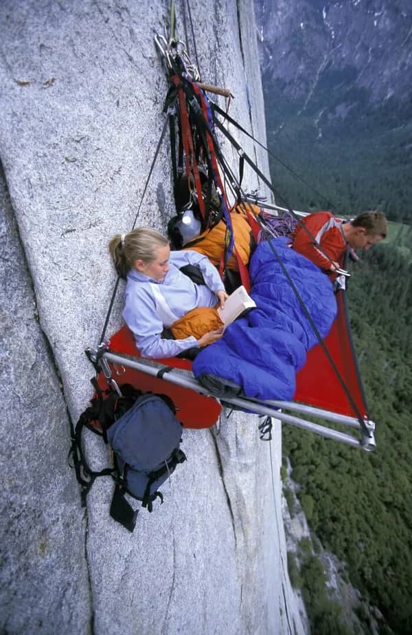 Couple on a portable portaledge suspended high up on a sheer granite cliff face.