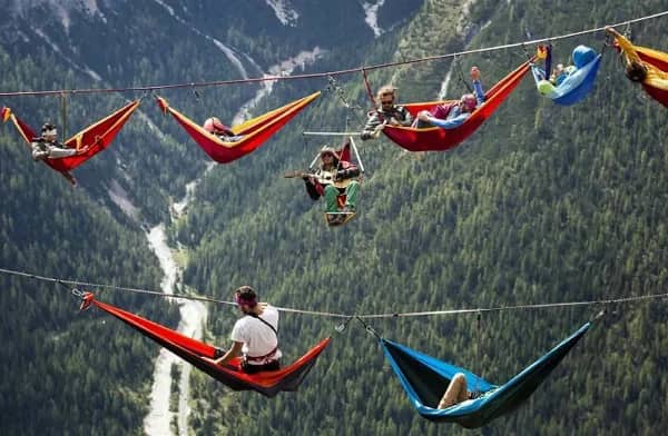 Long line of people relaxing in colorful hammocks strung over a vast mountain valley.