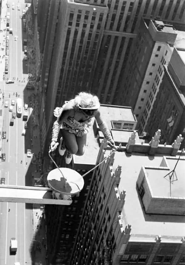 Vintage photo of a female aerial acrobat performing on a high beam over a city.
