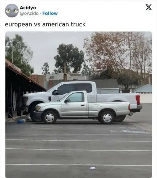 A small silver pickup truck parked in front of a massive white American pickup truck.