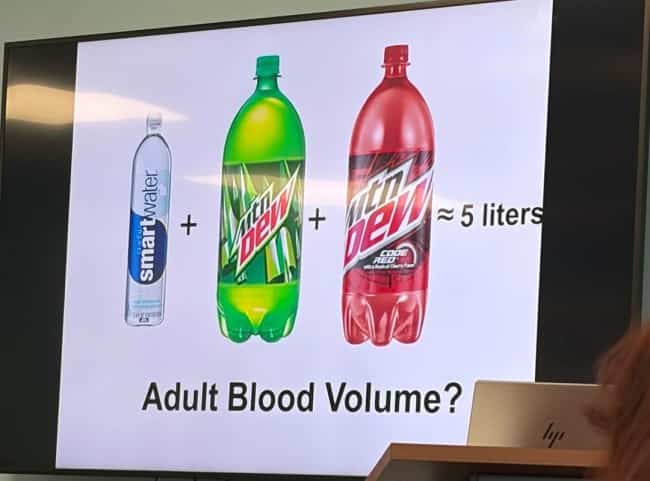A lecture presentation slide defining five liters of human blood using soda and water bottles.