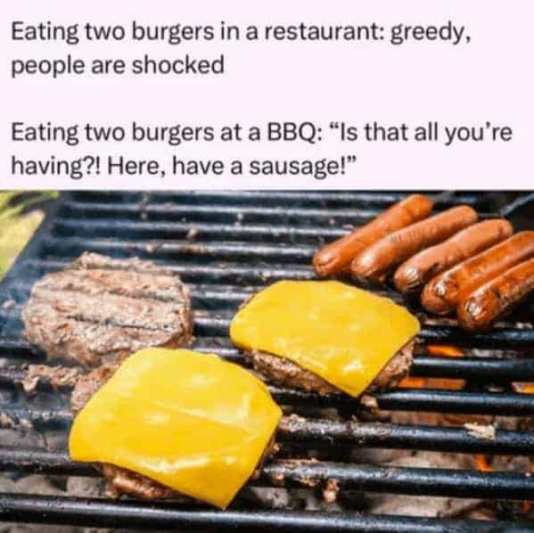 A food etiquette comparison grilling meme displaying cheese-covered hamburger patties and sausages sizzling on a fiery grill grate under text contrasting restrictive restaurant portion standards against welcoming barbecue culture.