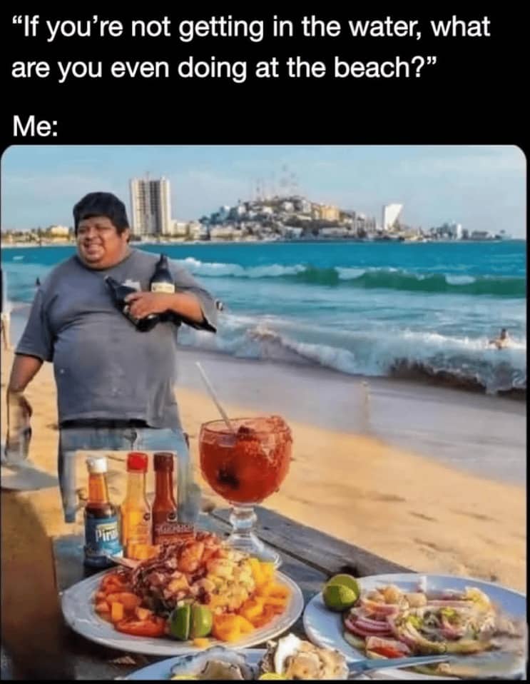 Man standing by a beach table filled with seafood and drinks, ignoring the ocean water.