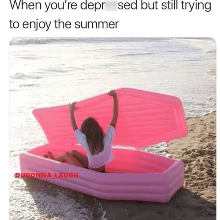 A woman sitting in a pink inflatable coffin-shaped pool float on the beach shore.