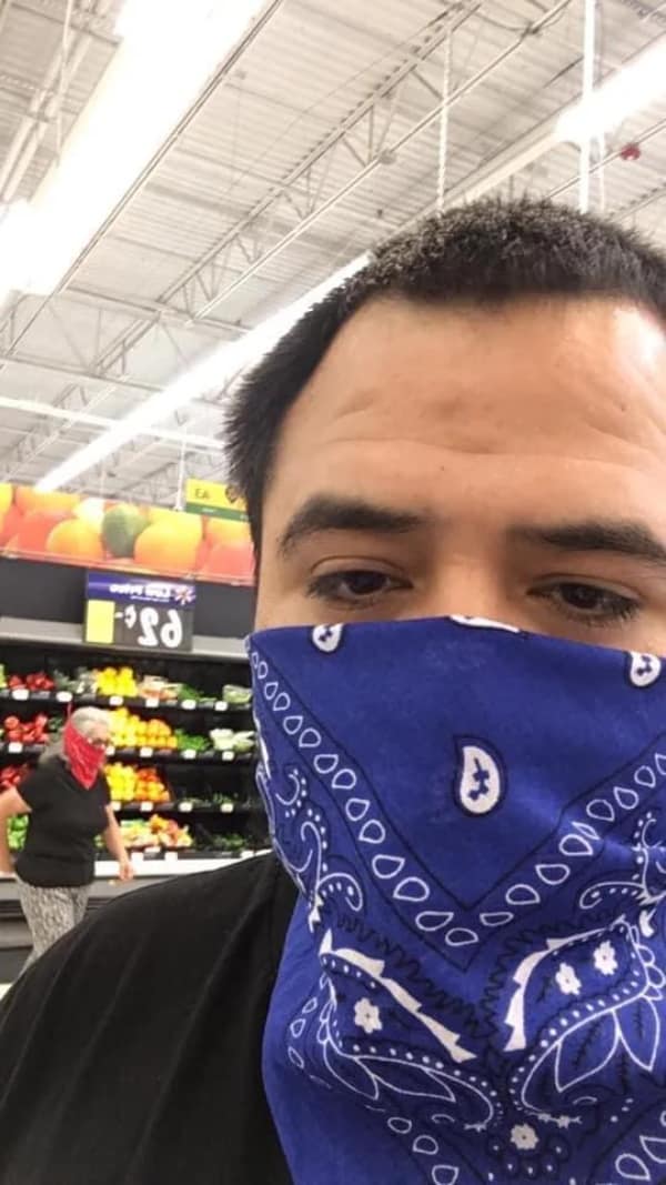 A supermarket produce aisle selfie showcases a viral blursed image coincidence where a man wearing a blue paisley bandana face mask stands near an elderly woman wearing a contrasting red bandana face mask.