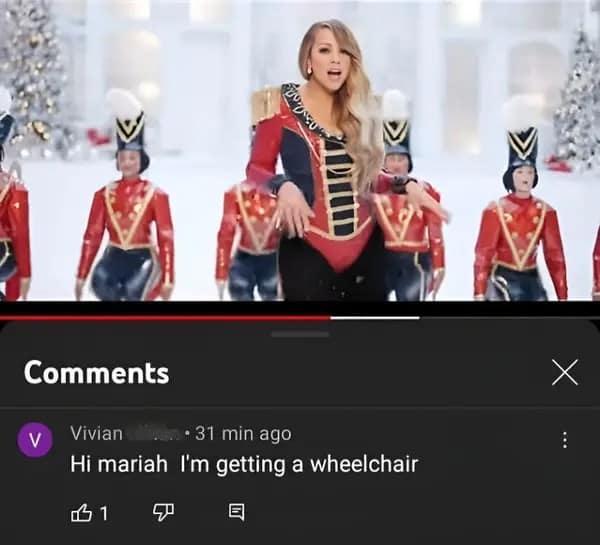 A screenshot of a Mariah Carey music video on YouTube showing her in a red soldier-style outfit. Below the video, a comment from a user named Vivian reads, "Hi mariah I'm getting a wheelchair." The comment has one "like" and feels entirely disconnected from the festive holiday content.