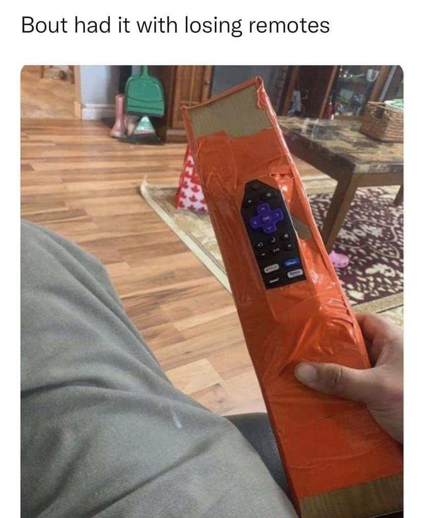 A purple Roku streaming TV remote control is wrapped heavily in neon orange duct tape and secured to a massive piece of shipping cardboard in a brilliant old memes solution to prevent losing it.