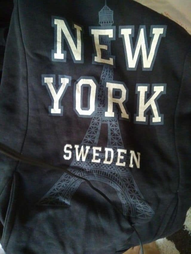 A clothing design failure operates as a viral classic meme showcasing a black hoodie printed with the graphic of the Eiffel Tower flanked by the completely mismatched text labels "NEW YORK" and "SWEDEN."