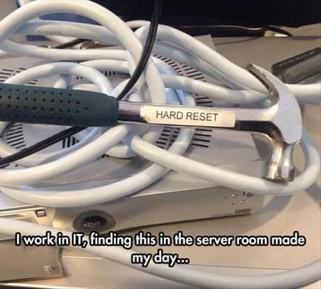 A humorous classic meme from an IT professional. A standard claw hammer rests on a pile of tangled white server cables, featuring a neat label-maker tag that simply says: "HARD RESET."