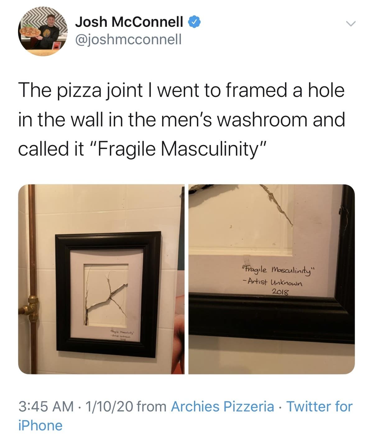 A classic meme photo of a framed, shattered hole in a restroom wall at a pizza joint, accompanied by a small plaque that reads "'Fragile Masculinity' - Artist Unknown, 2018."