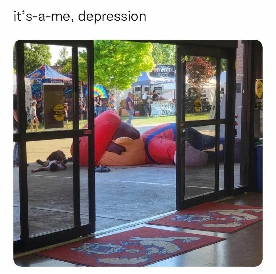 A giant inflatable Super Mario figure lies deflated face-down on the ground outside a fair pavilion, capturing a legendary classic meme with the text caption "it's-a-me, depression".