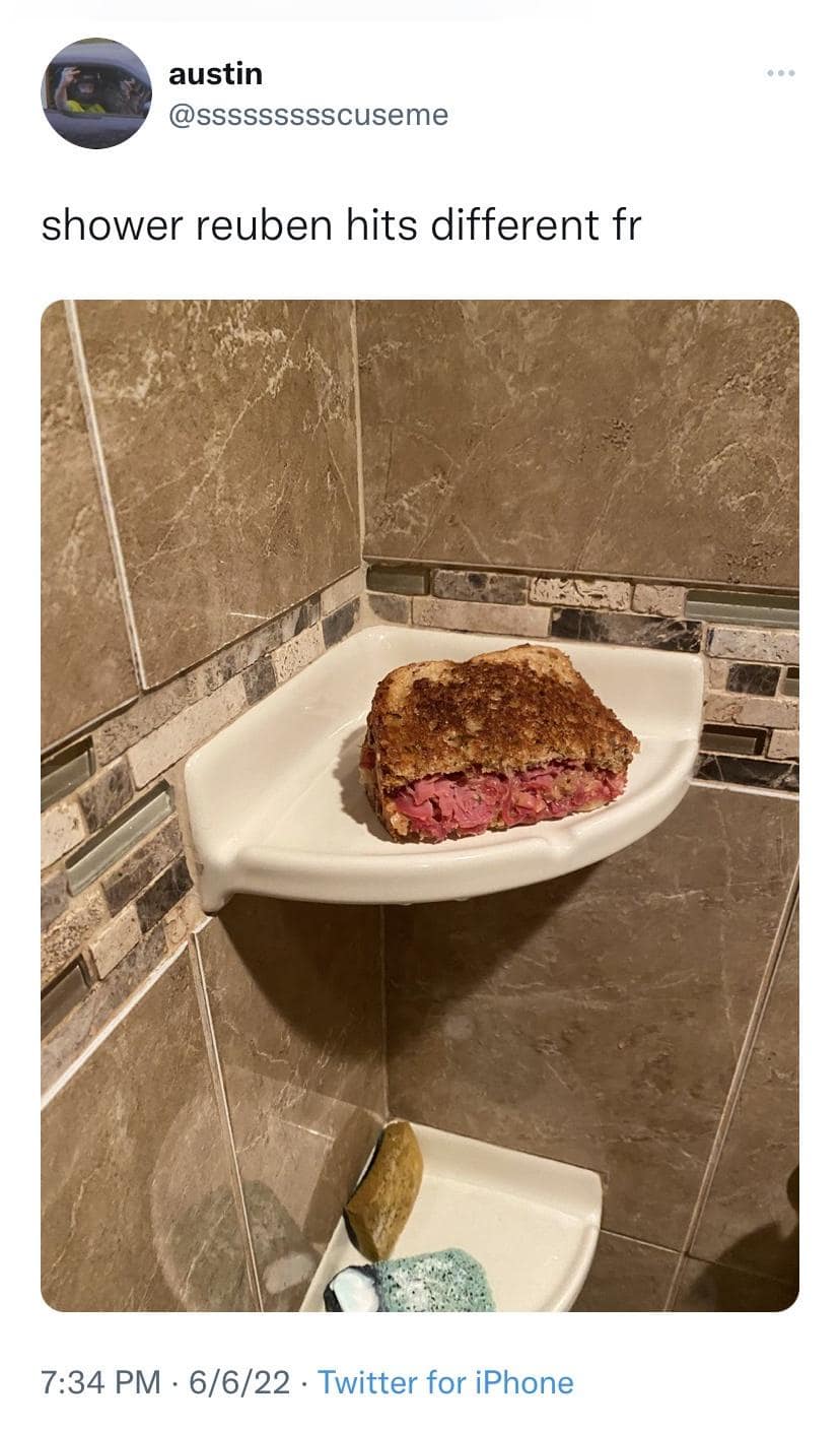 A social media snapshot features a fully loaded, toasted corned beef Reuben sandwich resting bizarrely on a white ceramic corner soap shelf inside a tiled bathroom shower stall, shared as a classic meme captioned "shower reuben hits different fr".