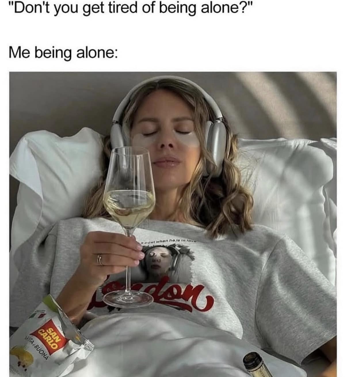 A classic meme contrasting the judgmental question "Don't you get tired of being alone?" with a photo of a woman in total bliss, wearing eye patches and high-end headphones while holding a glass of wine in bed.