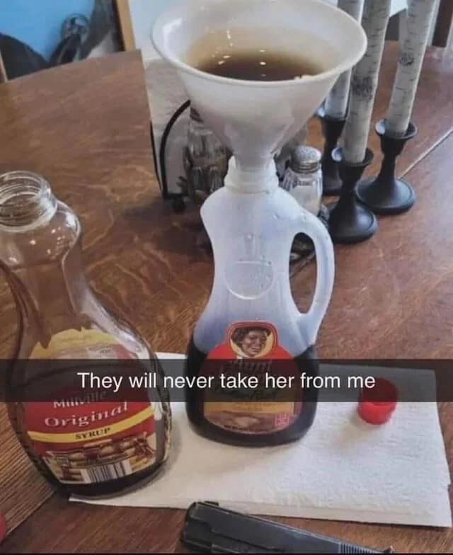 Someone funneling syrup into a discontinued Aunt Jemima bottle next to a handgun, referencing a controversial classic meme regarding brand rebranding.