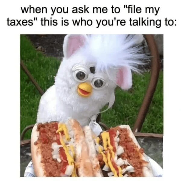 A deeply relatable classic meme featuring a wide-eyed, white Furby sitting at a table in front of two massive chili dogs, representing the absolute chaos of trying to "file taxes" as a functional adult.