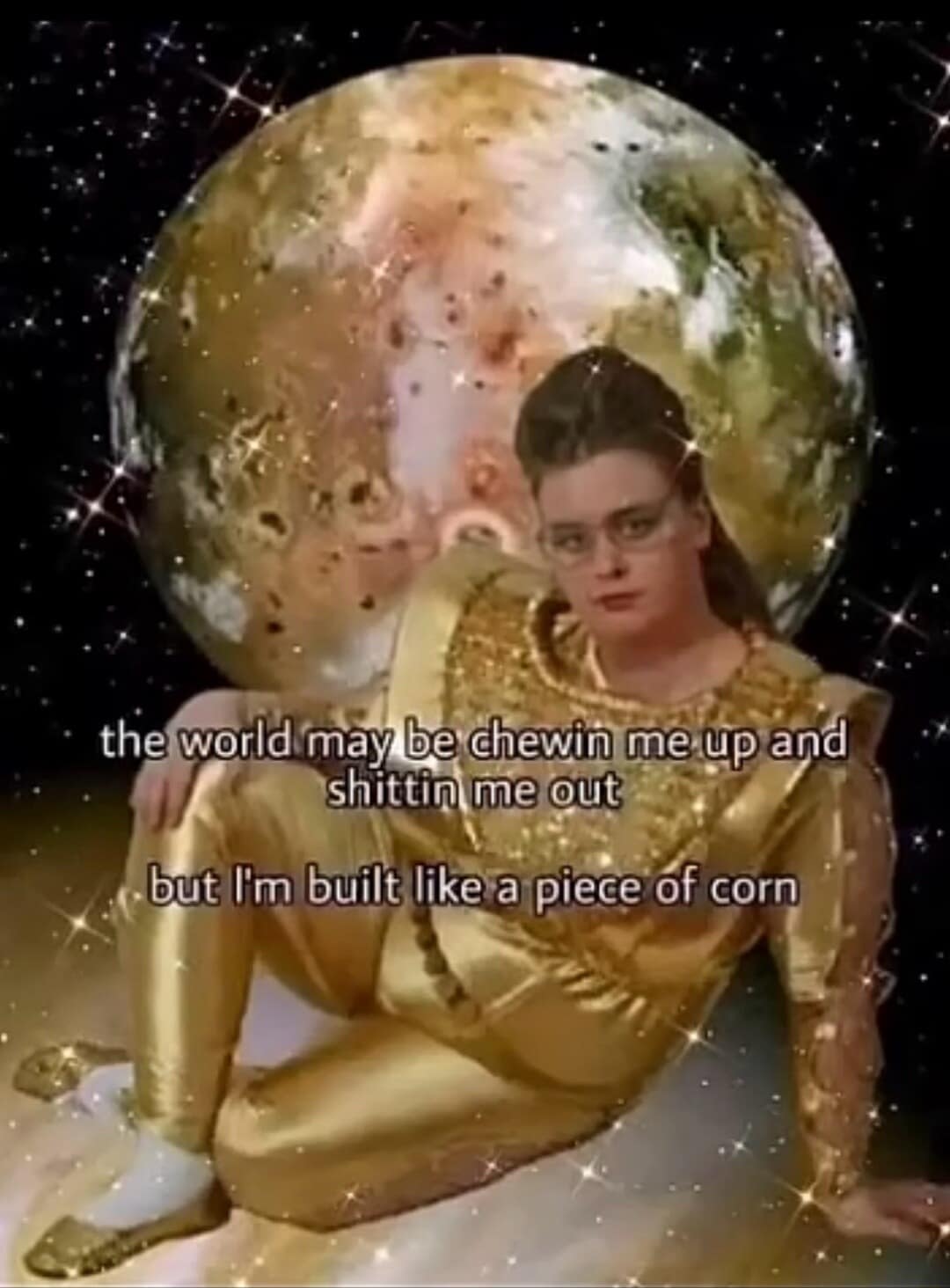 A cosmic classic meme showing a woman in a metallic gold space suit lying on a sparkly lunar surface, stating that while the world may chew her up and spit her out, she is "built like a piece of corn."