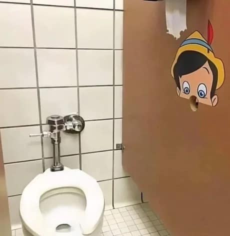 A cursed image classic meme from a public bathroom stall where a sticker of Pinocchio has been placed so that the toilet paper holder hole serves as his nose, looking directly at the toilet.