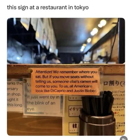 A classic meme displaying an orange printed warning sign taped to a wooden restaurant counter in Tokyo that instructs customers not to swap seats because "To us, all Americans look like DiCaprio and Justin Bieber."