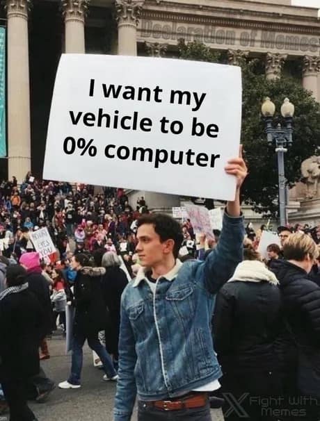 A protestor in a denim jacket holds up a large white poster board stating a desire for a vehicle to be zero percent computer in an anti-technology classic meme.