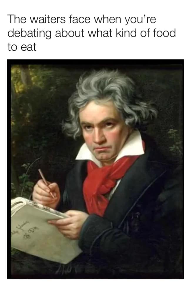 A stern portrait of Ludwig van Beethoven holding a pen and paper with a judgmental glare, used as a classical art meme about an impatient waiter waiting for a customer to order.