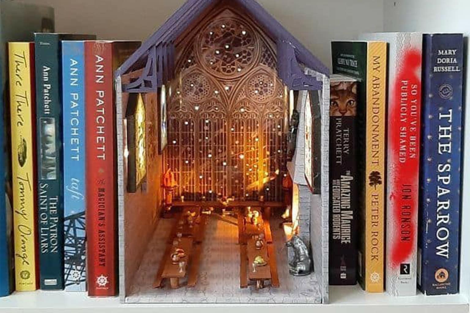 Cool bookends gallery showcasing the intricate art of book nooks, featuring an enchanted forest with fairy lights, an infinite library with white marble columns, and a wizarding school's grand staircase covered in miniature portraits.