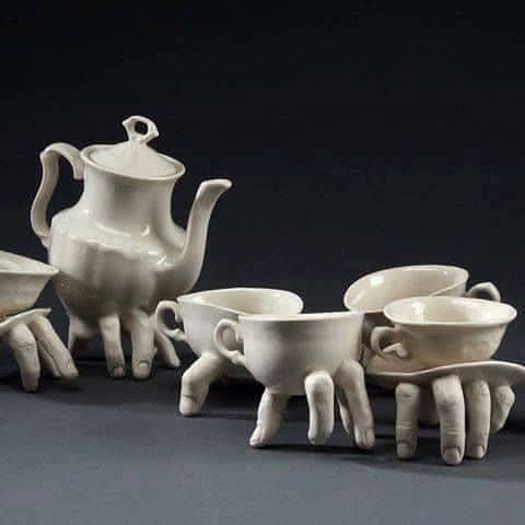 A porcelain tea set where the teapot and cups stand on realistic ceramic human fingers.