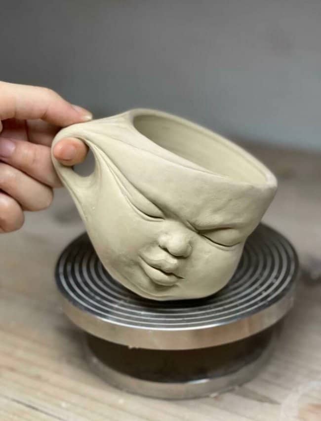 A light-colored ceramic mug with a squished human face that appears to be grimacing.