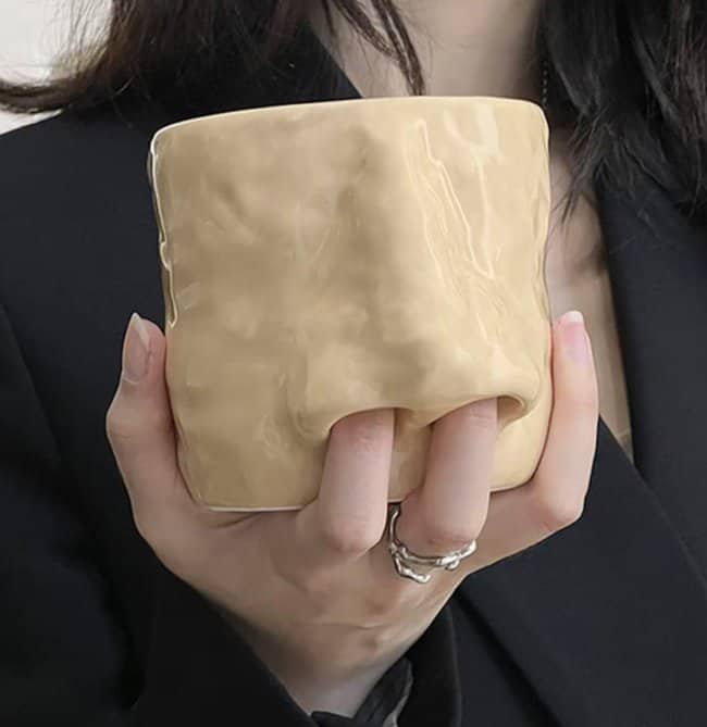 A hand holding a tan mug with two finger-shaped indentations where the nostrils would be.
