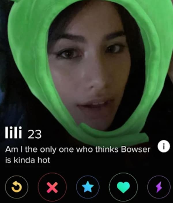 A funny dating app profile card for 23-year-old lili showcases her face inside a bright lime-green plush character hood with a bio that asks, "Am I the only one who thinks Bowser is kinda hot".