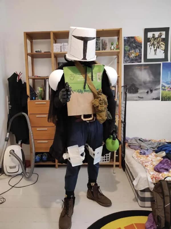 cursed cosplay of the Mandalorian featuring a white plastic bucket for a helmet, paper bags for a chest plate, and white kitchen bowls for shoulder armor.