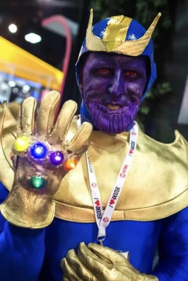 A detailed but budget cursed cosplay of Thanos, with heavy purple face paint, gold duct tape armor, and an Infinity Gauntlet fitted with actual glowing LED lights.