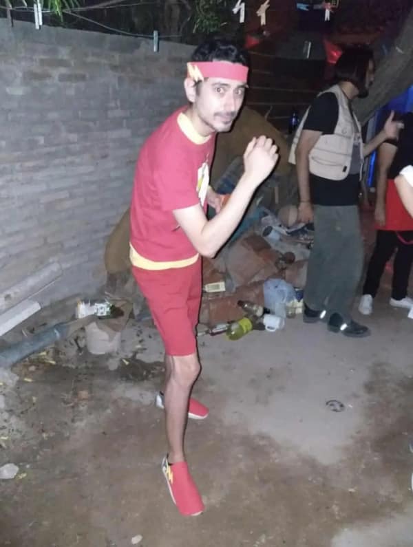 A minimalist cursed cosplay of The Flash featuring a man in an all-red outfit with yellow paper lightning bolts taped to his headband, chest, and shoes.