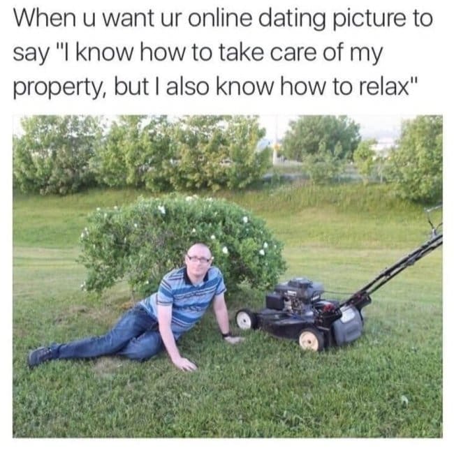 A middle-aged man striking a dramatic, glamorous pose on his side in the grass directly next to a push lawnmower highlights a popular dating app meme about balancing domestic chores with a relaxed lifestyle.