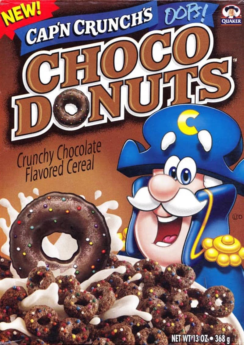 A vintage chocolate-brown box of Cap'n Crunch's Oops! Choco Donuts cereal captures a rare flavor variant in the history of discontinued cereals, showing the Cap'n presenting donut-shaped pieces covered in colorful sprinkle