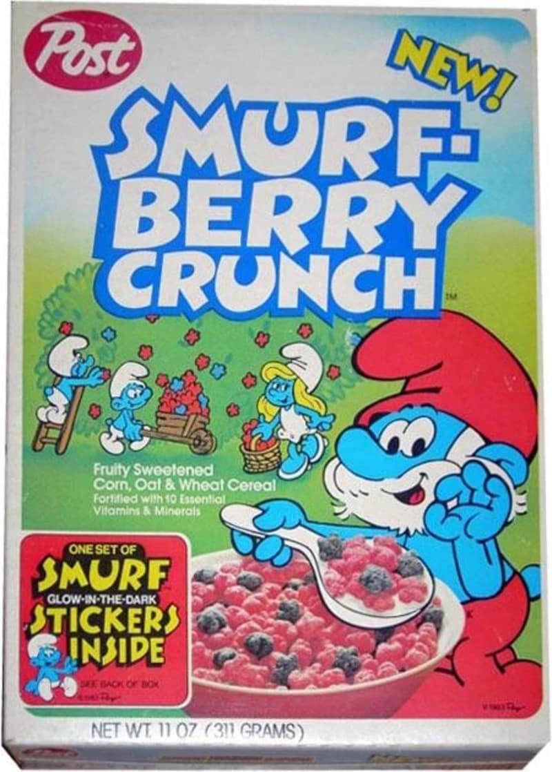 A vintage 1980s box of Post Smurf-Berry Crunch highlights an iconic nostalgic cereal, showing Papa Smurf enjoying a bowl of bright pink and purple berry-shaped cereal pieces with a glow-in-the-dark sticker promo.