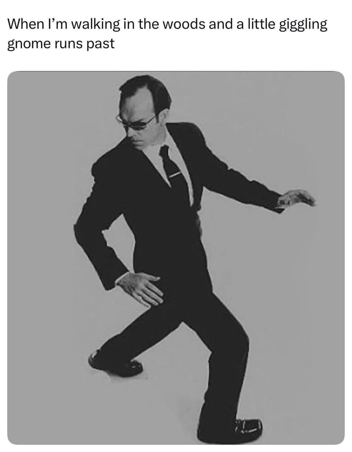 A funny dnd meme featuring a man in a black suit looking alert and suspicious in the woods, representing a player’s immediate "combat mode" when a giggling gnome runs past.