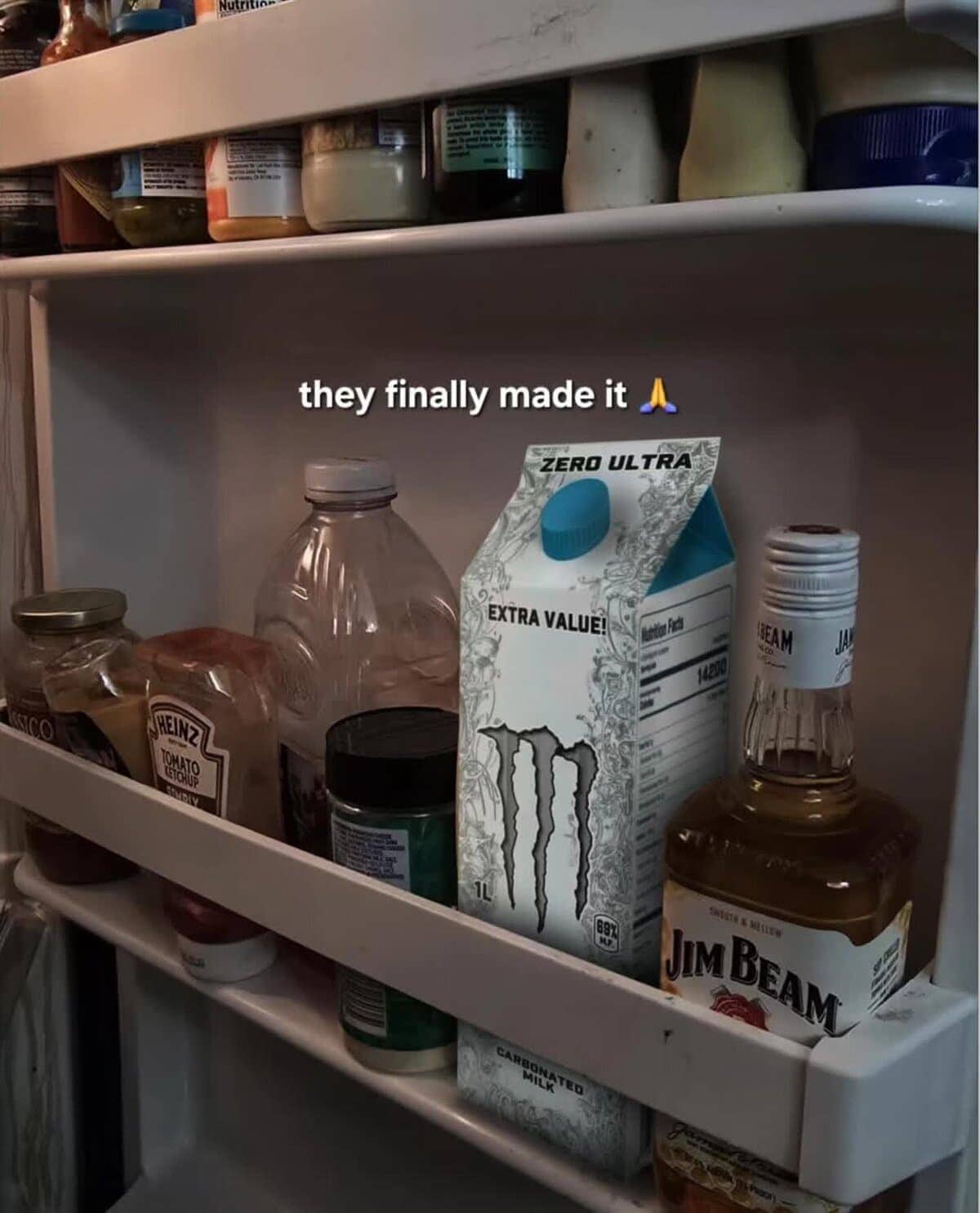 Refrigerator door shelf holding ketchup, Jim Beam whiskey, and a Monster Energy milk carton.