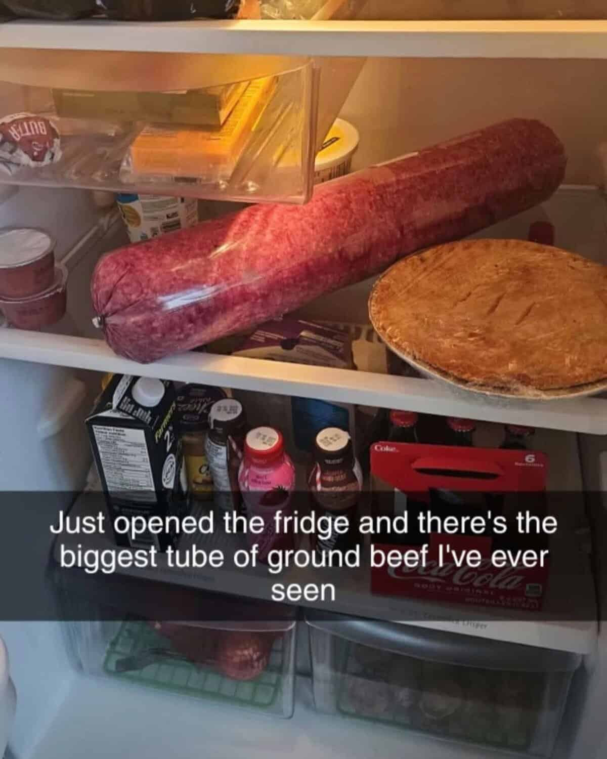 Refrigerator shelf holding a giant plastic tube of ground beef and a whole pie.
