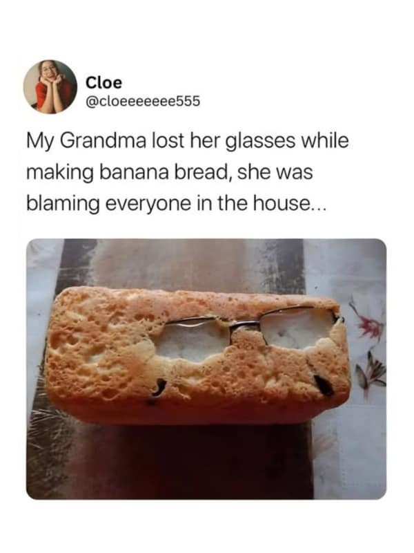 A golden-brown loaf of baked banana bread has a pair of wire-rimmed reading glasses accidentally baked directly into its top crust, anchoring a viral dessert meme.