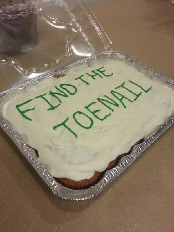 A homemade sheet cake with thick vanilla frosting inside an aluminum foil pan features a horrifying prank message written in green icing that reads "FIND THE TOENAIL" in a dark humor food meme.